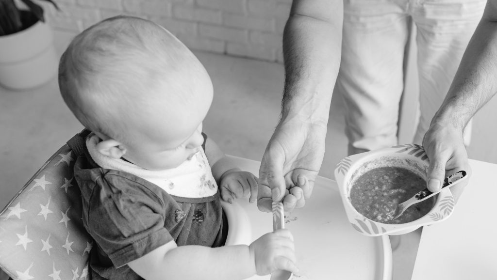 Close up of baby in high chair grabbing spoon.